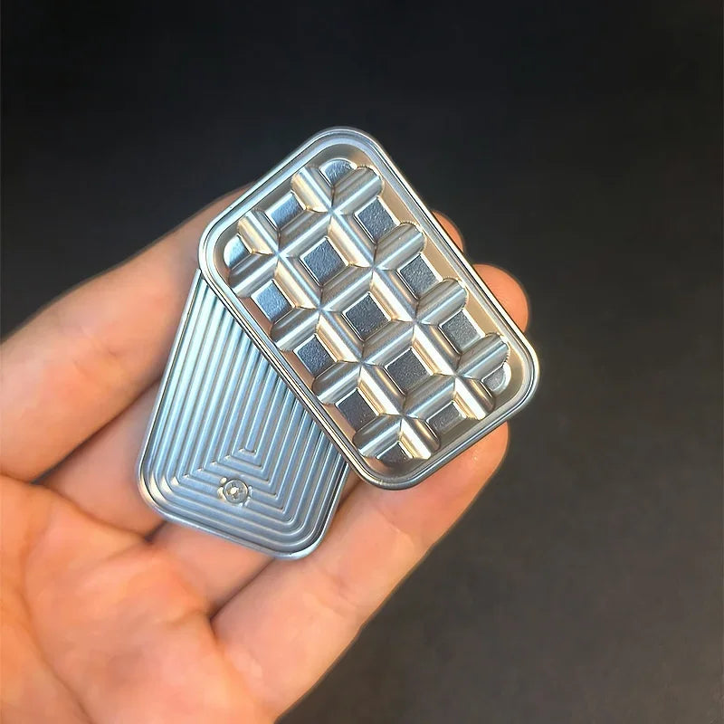 Hand holding a rectangular metal fidget slider with geometric pattern on dark background
