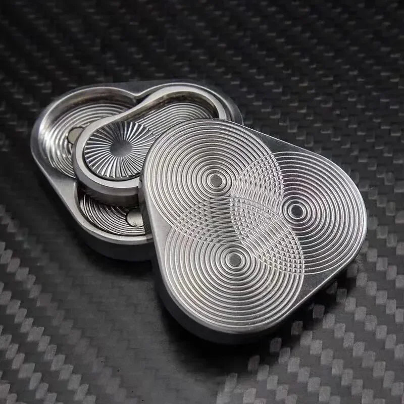 Metal fidget slider with intricate circular pattern on carbon fiber surface