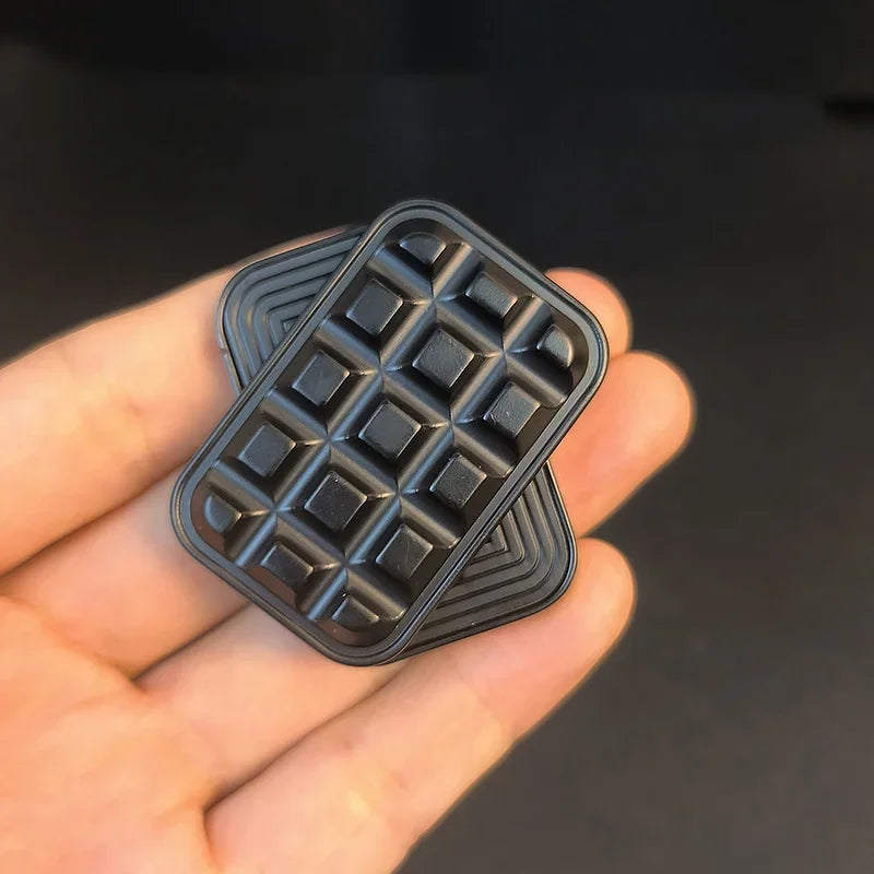 Black metal fidget toy with textured geometric pattern held in hand