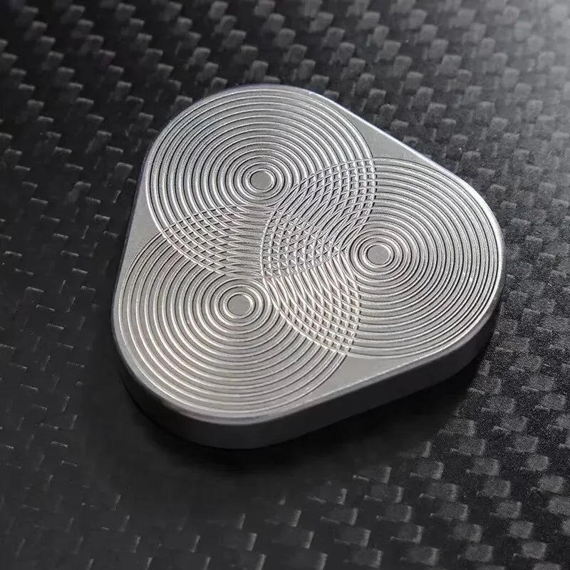 Silver metal fidget spinner with geometric pattern on a black carbon fiber surface