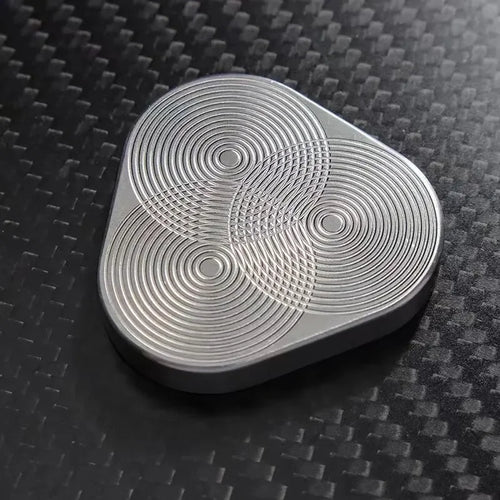 Silver metal fidget spinner with geometric pattern on a black carbon fiber surface